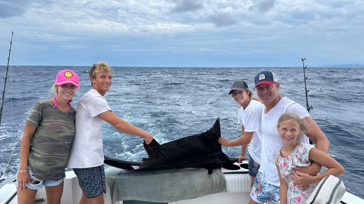 Family posing with a sailfish on the deck before releasing it on a fishing charter in Nuevo Vallarta